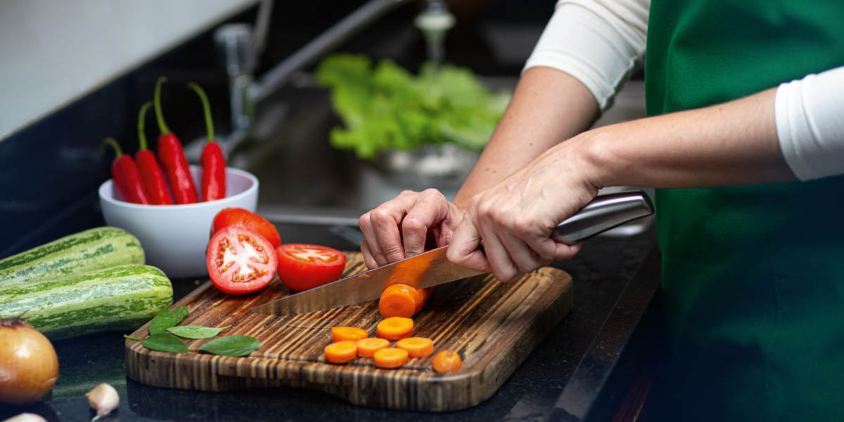 Una mujer cortando verduras frescas en una tabla de madera.