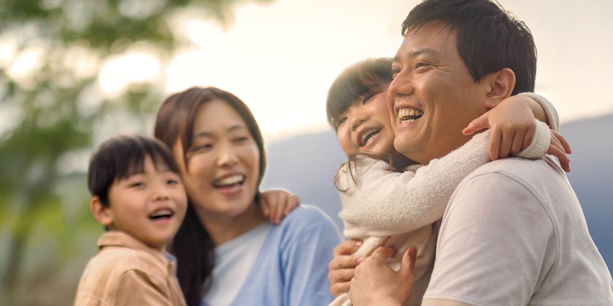 A father and mother joyfully holding their young daughter and son as they spend time together outdoors.