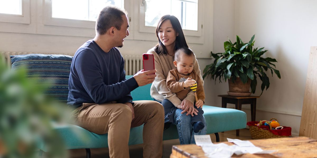 A husband showing his wife something on a smartphone while she holds their young son.
