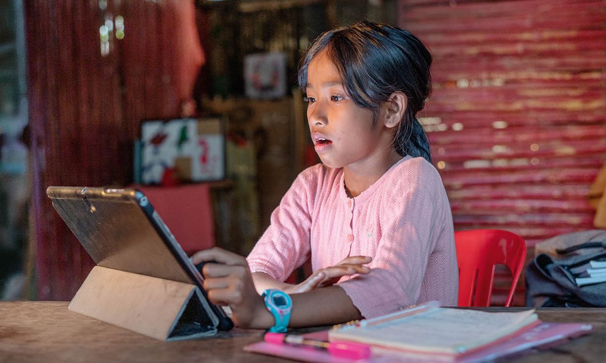 A young girl looking shocked at something on her tablet while she does her homework.