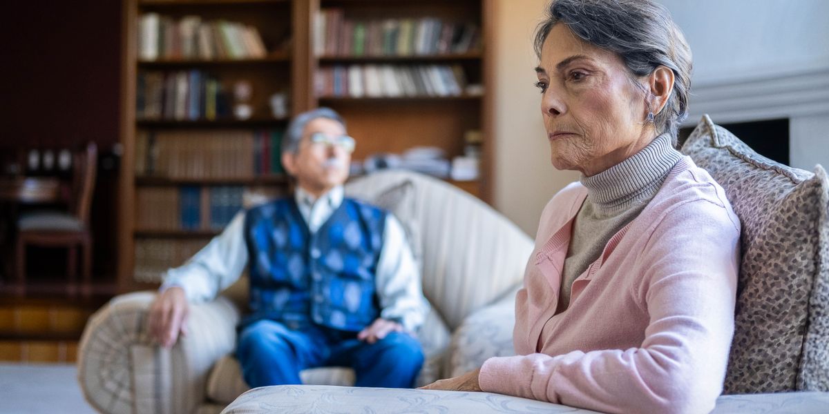 An unhappy older couple sitting apart from each other. They both stare off into the distance.
