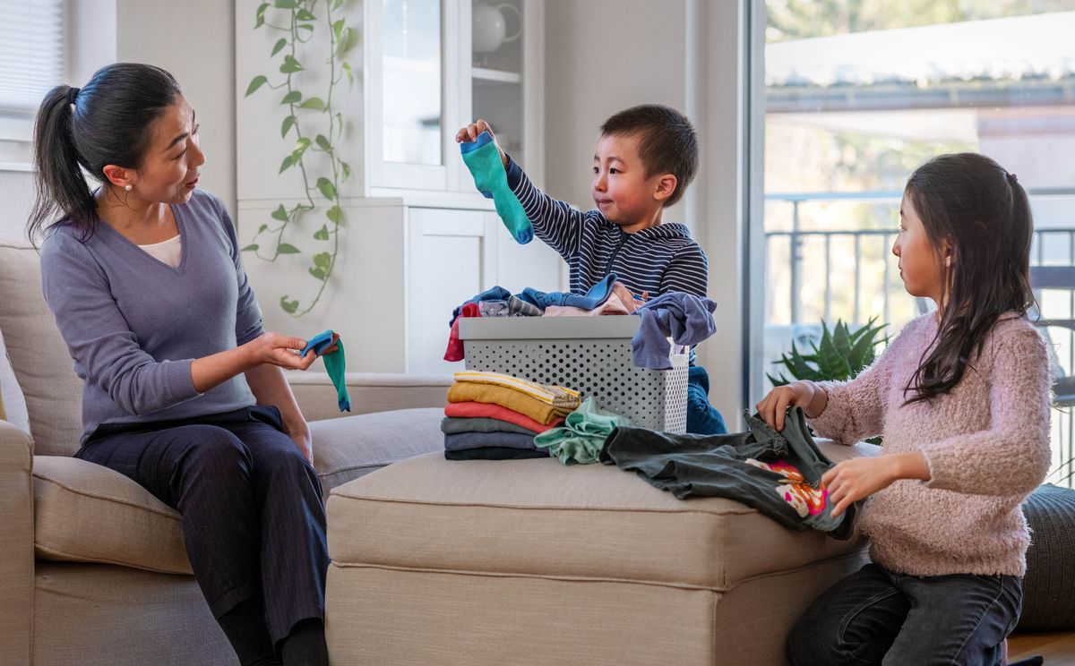 A mother teaching her young children how to sort and fold laundry. Her son hands her a matching sock while her daughter folds a T-shirt.