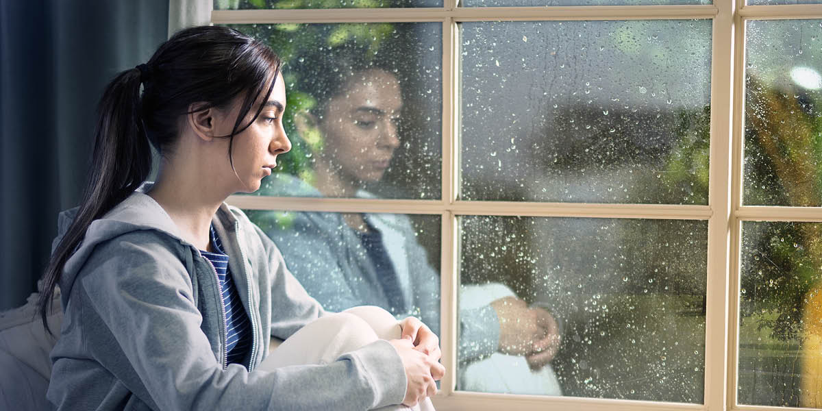 A depressed teenage girl staring out a window at the rain.