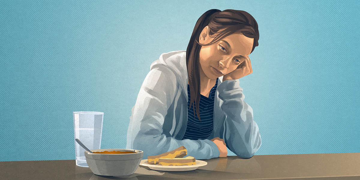 An ill teenage girl staring blankly. She is not eating the meal set before her.