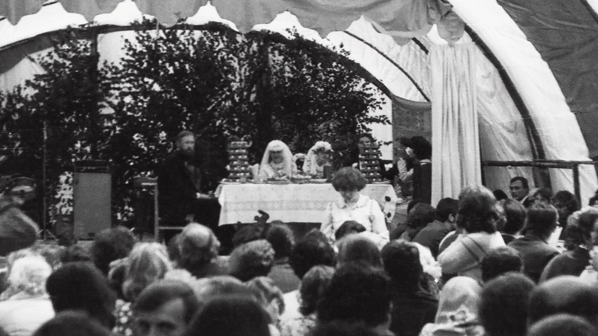 The Pudžiuvys’ wedding taking place on a platform under a large tent. They sit at a table with Virgilijus’ cousin and her husband, who also got married on the same day.