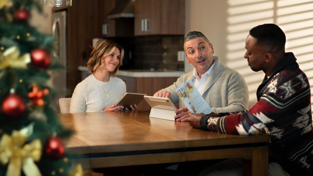 The couple from the previous image, studying the “Enjoy Life Forever!” brochure with the man at his home. The Christmas tree is nearby.
