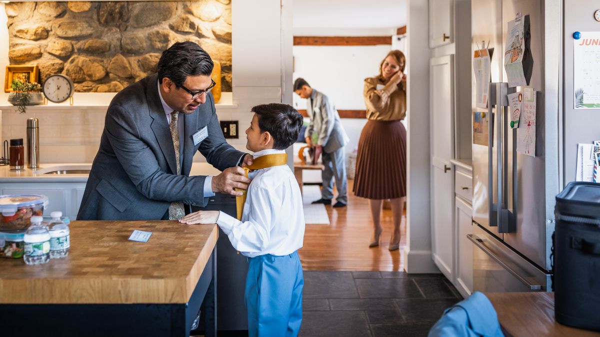 A family happily preparing to leave their home for a convention. The father helps his younger son tie his necktie while his wife and older son get ready.