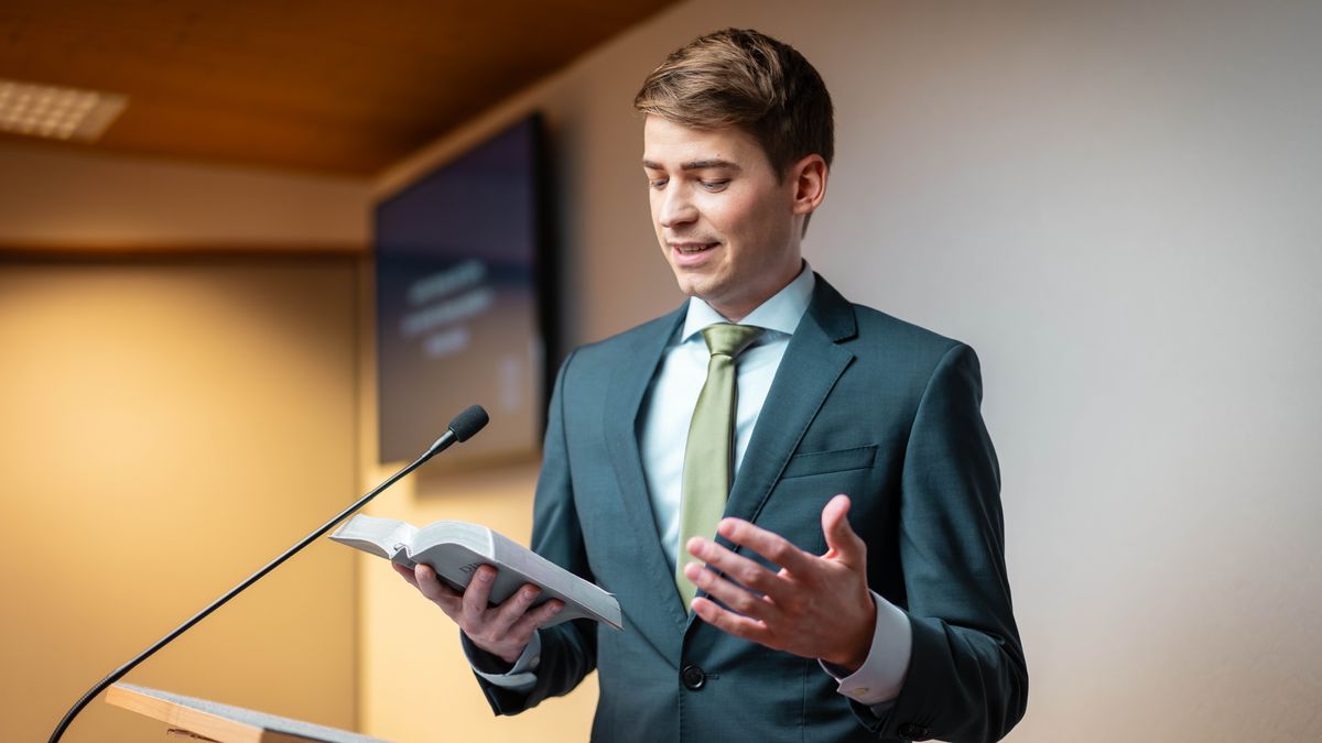 The young brother reads the Bible from the platform during a congregation meeting.