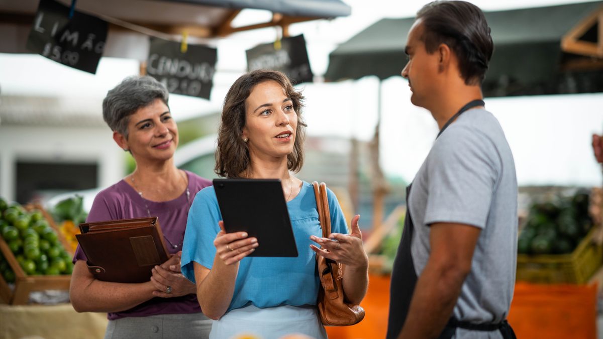 The two sisters speaking with another man at a market. The sister who earlier struggled to give a witness now speaks confidently to the man.