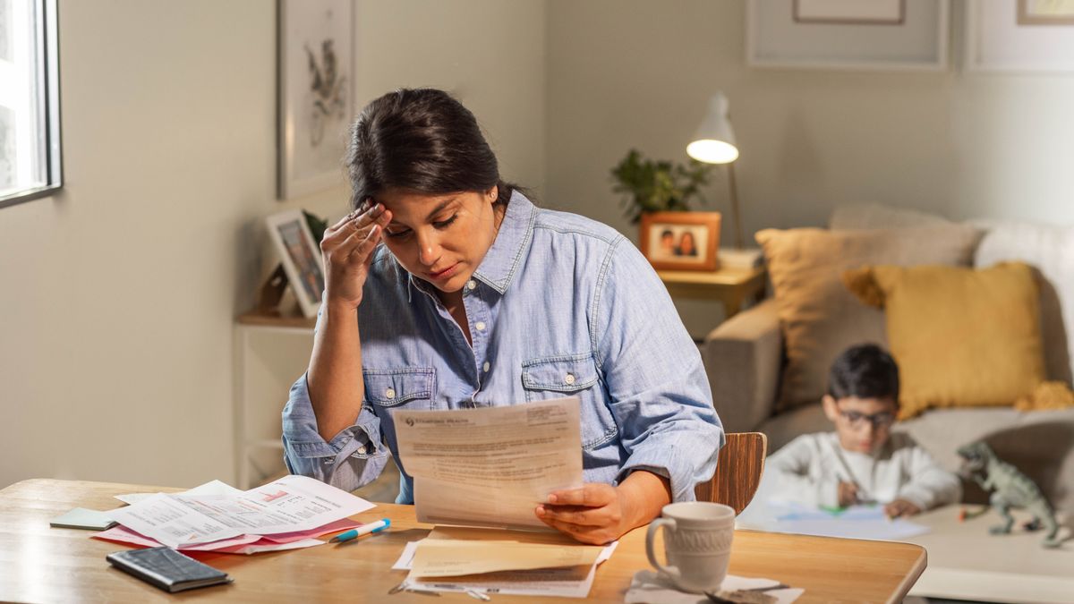 The single mother anxiously going through a stack of bills while her son plays behind her.