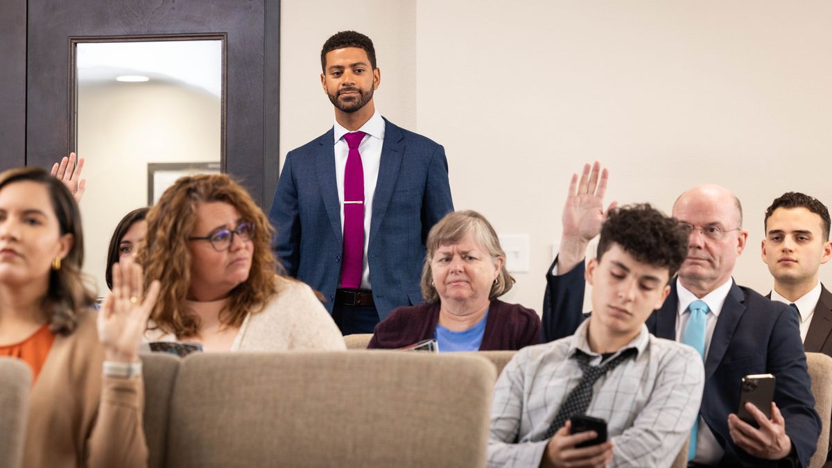 The brother observes the son during a meeting. The son seems disinterested as he slouches in his seat and looks at his phone.