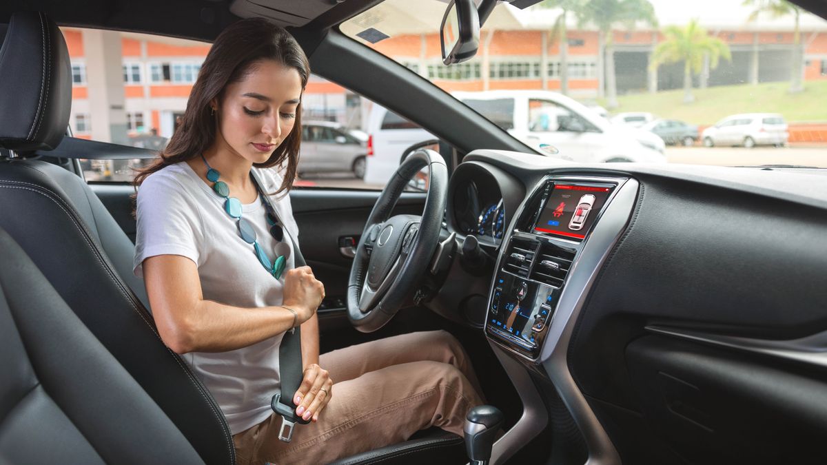 A sister buckles her seat belt before driving her car.
