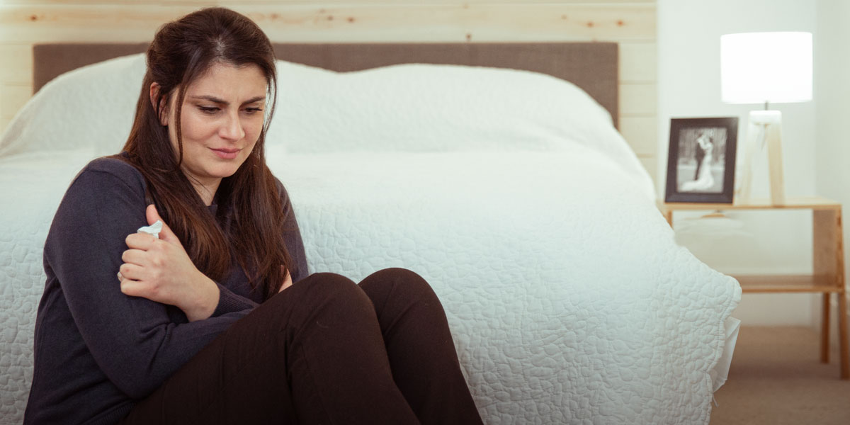 خواهری روی زمین کنار تختش نشسته و گریه می‌کند.‏ عکس عروسی‌شان پشت سر دیده می‌شود.‏