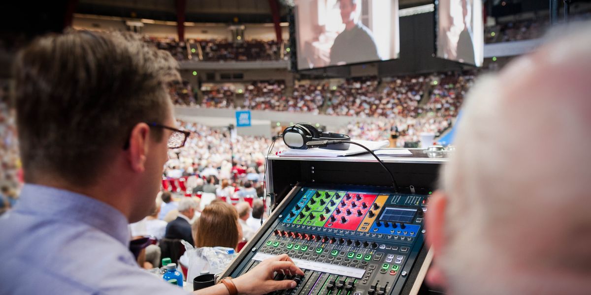 Lors d’une assemblée régionale, un frère ajuste le volume tandis que l’auditoire regarde une vidéo sur des écrans géants.