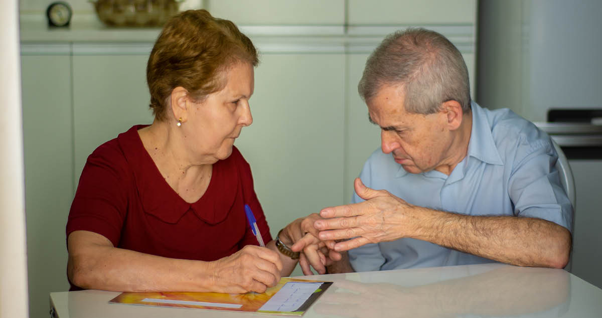 Maria Lúcia écrit une lettre tandis que José Antônio lui signe dans la main gauche.