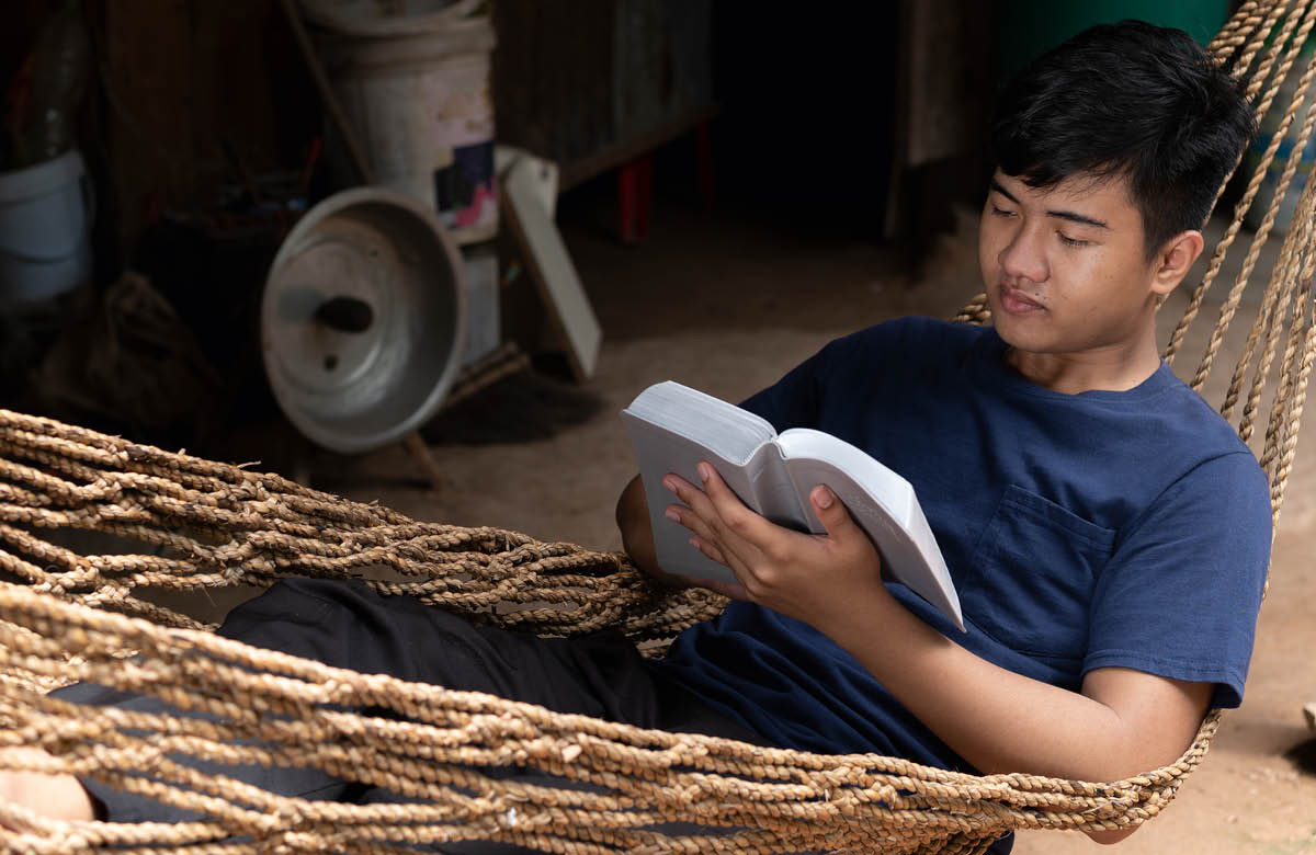 Allongé dans un hamac, un adolescent lit la Bible.