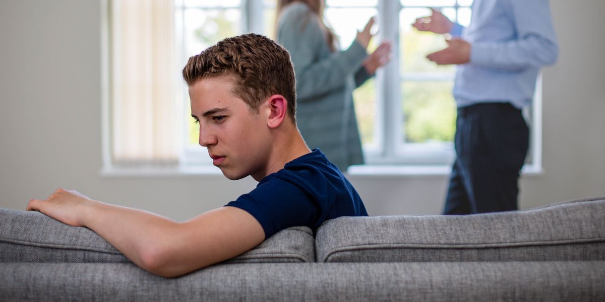 Un adolescent triste détourne le regard tandis qu’à l’arrière-plan ses parents se disputent.