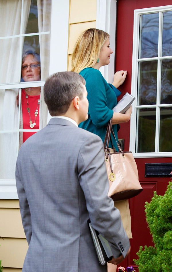 Une femme regarde par la fenêtre des Témoins de Jéhovah qui frappent à sa porte.