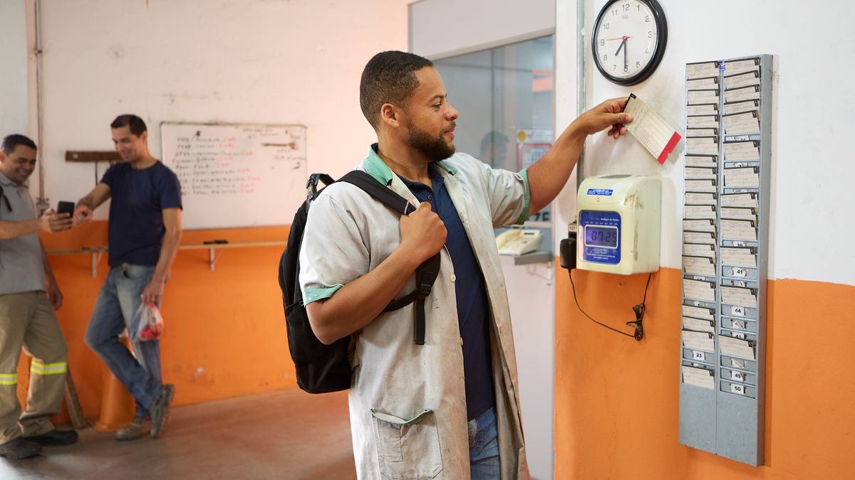 Un frère arrive au travail à 7h29. En arrière-plan, on voit des collègues qui regardent quelque chose sur un téléphone portable.