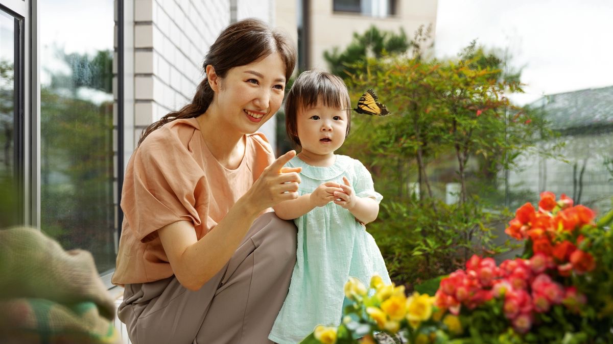 En bas de leur immeuble situé en pleine ville, une maman montre un papillon à sa petite fille.