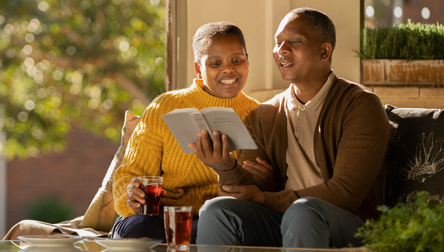 Lánúin phósta ag léamh an Bhíobla le céile sa bhaile agus iad ag ithe sólaistí.