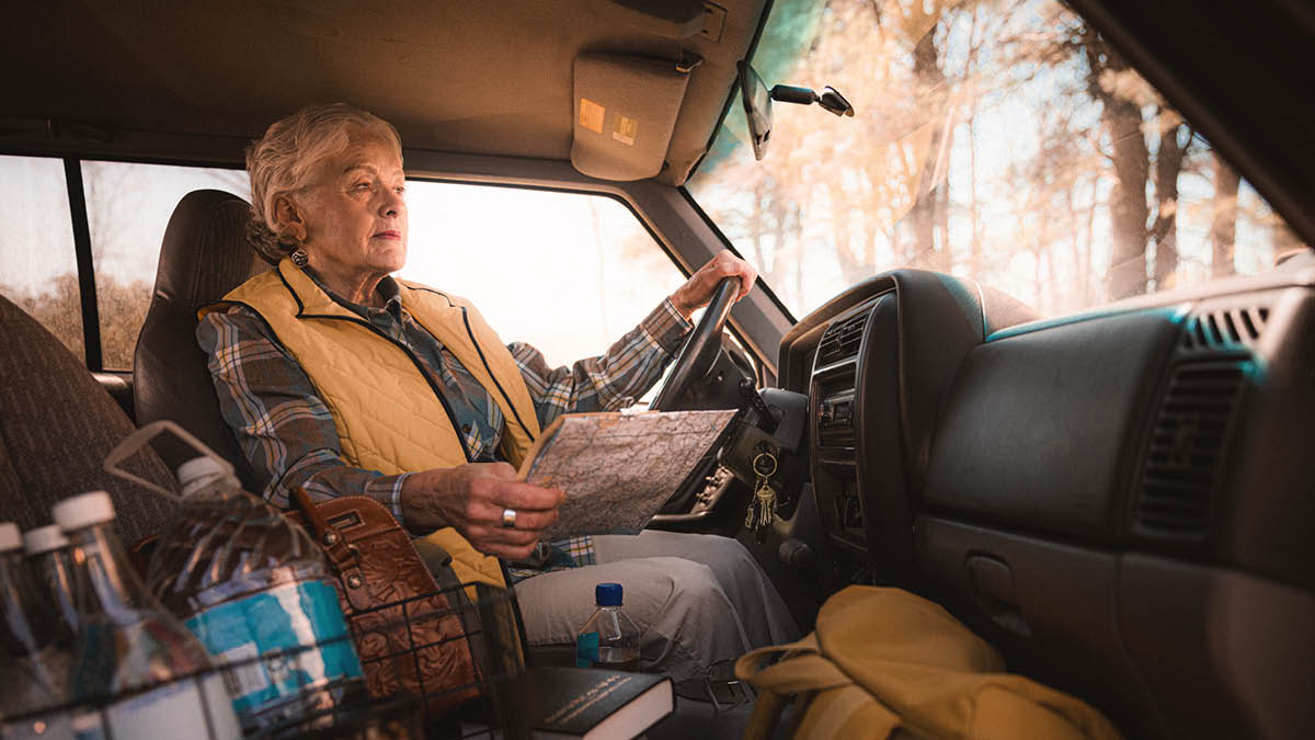 Eine Schwester sitzt im Auto und hält eine Straßenkarte in der Hand. Sie hat Wasserflaschen und andere Vorräte dabei.