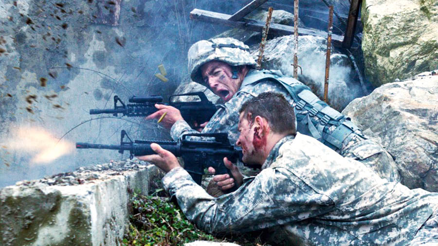 In einem Gefecht schießen Soldaten im Schutz einer Mauer.