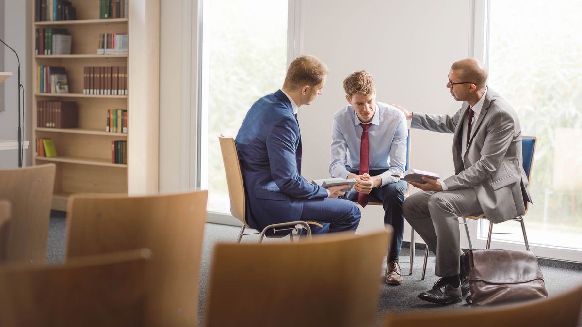 Dos ancianos de la congregación le muestran con bondad unos versículos de la Biblia a un joven. Uno de los ancianos le pone la mano en el hombro al joven mientras habla con él.