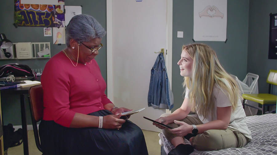 Una imagen del video “La alegría de hacer discípulos. Aceptemos la ayuda de Jehová: Nuestros hermanos”. La hermana mayor estudia la Biblia con Coral mientras Rita está de viaje.