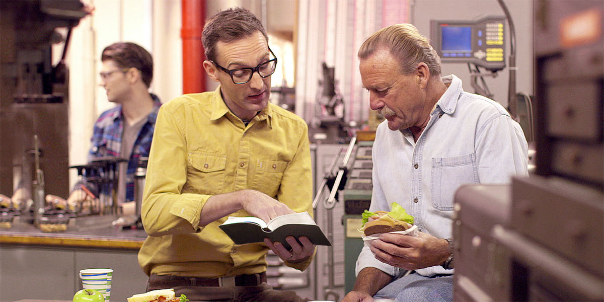 Ib tug kwvtij nyeem ib nqes Vajlugkub rau ib tug txivneej tom tsev haujlwm.