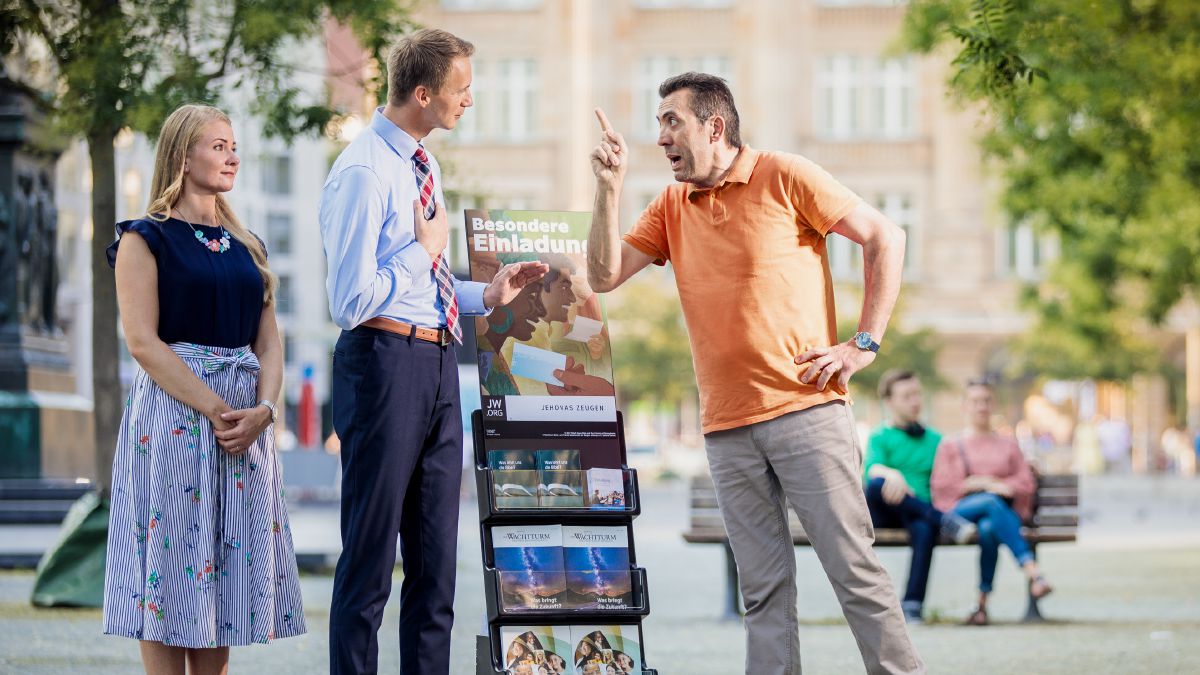 Egy férfi gorombán viselkedik egy házaspárral, akik a tanúskodóállványnál állnak, de ők szelídek maradnak