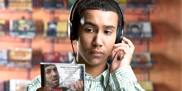 Yon adolesan ki ak kas nan zòrèy li k ap koute yon mizik pandan l ap egzamine enfòmasyon ki nan po CD a.