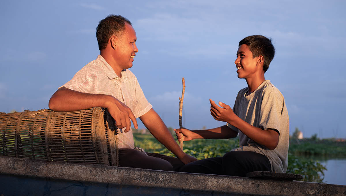 Seorang ayah dan anak laki-lakinya yang remaja mengobrol dengan akrab di atas perahu.