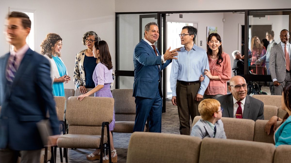 Young and old brothers and sisters wey come from different place de talk before meeting start. One brother de welcome one husband and wife wey come meeting for their first time.