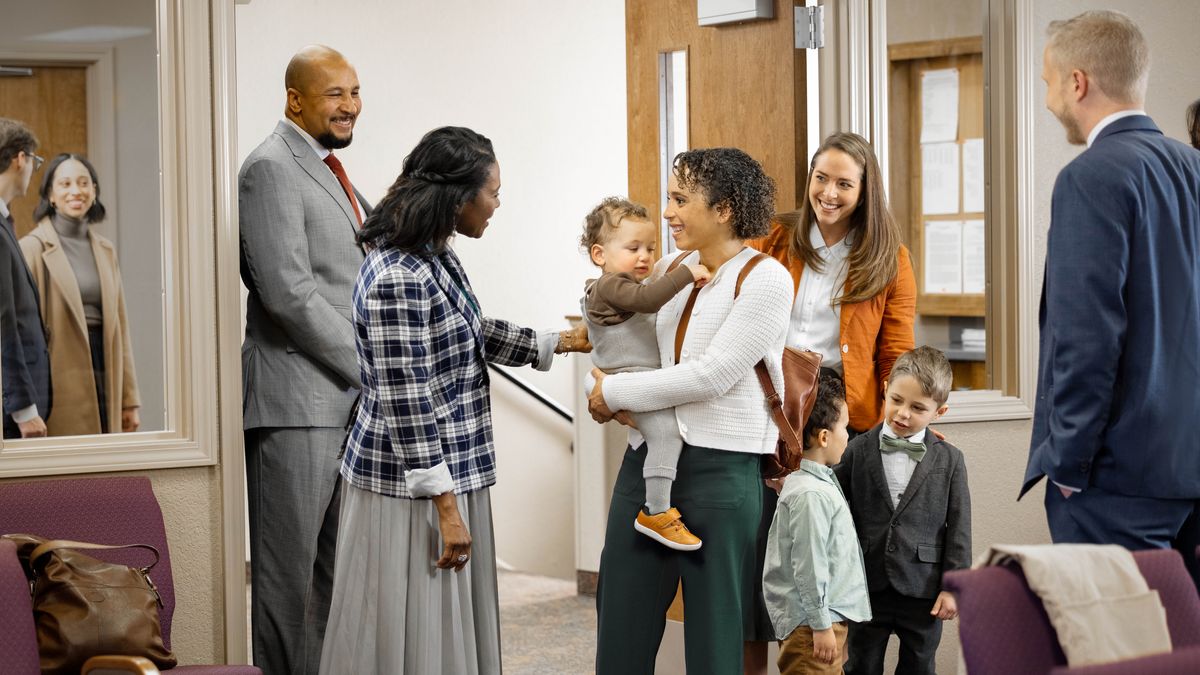 The woman for the other picture de happy as brothers and sisters de welcome-am for Kingdom Hall. E carry im small pikin for hand and im other pikin de talk to one young boy.
