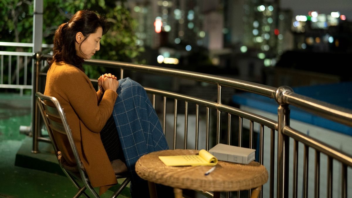 A sister praying while sitting on the rooftop of her home at night. Next to her on a table is a Bible and a notepad.
