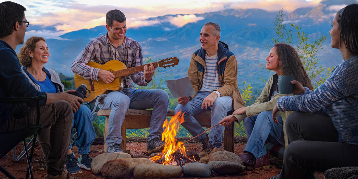 Aggagayyem nga agduduma ti edadda a nakatugaw iti aglikmut ti campfire. Aggitgitara ti maysa kadakuada.