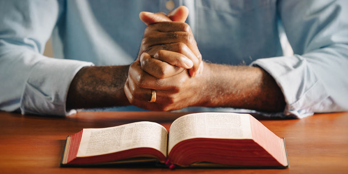 Lalaki nga agkarkararag a nagpinnetpet dagiti imana. Nakalukat ti Bibliana iti lamisaan iti sangona.
