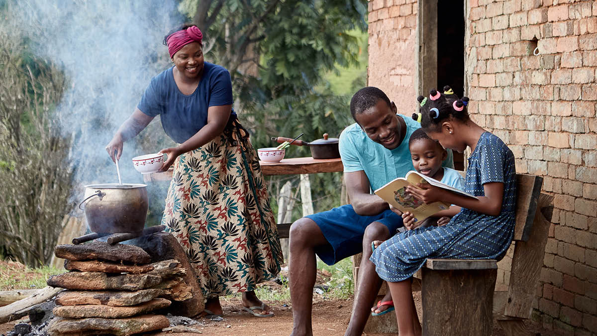 Naragsak a pamilia iti ruar ti simple a balayda. Aglutluto ti nanang iti simple a kanenda. Iti asideg, iyad-adal ti ama ti libro a “Dagiti Leksion a Masursurom iti Biblia” iti dua nga annakda.