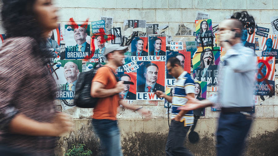 Tattao a lumablabas iti pader a napno kadagiti poster dagiti agkamkampania a politiko.