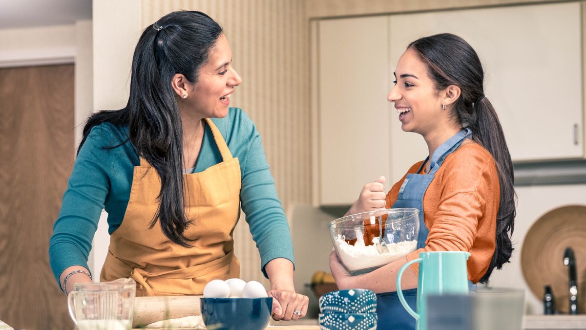 Seorang ibu dan anak perempuannya mengobrol sambil menyiapkan makanan. Mereka terlihat bahagia.
