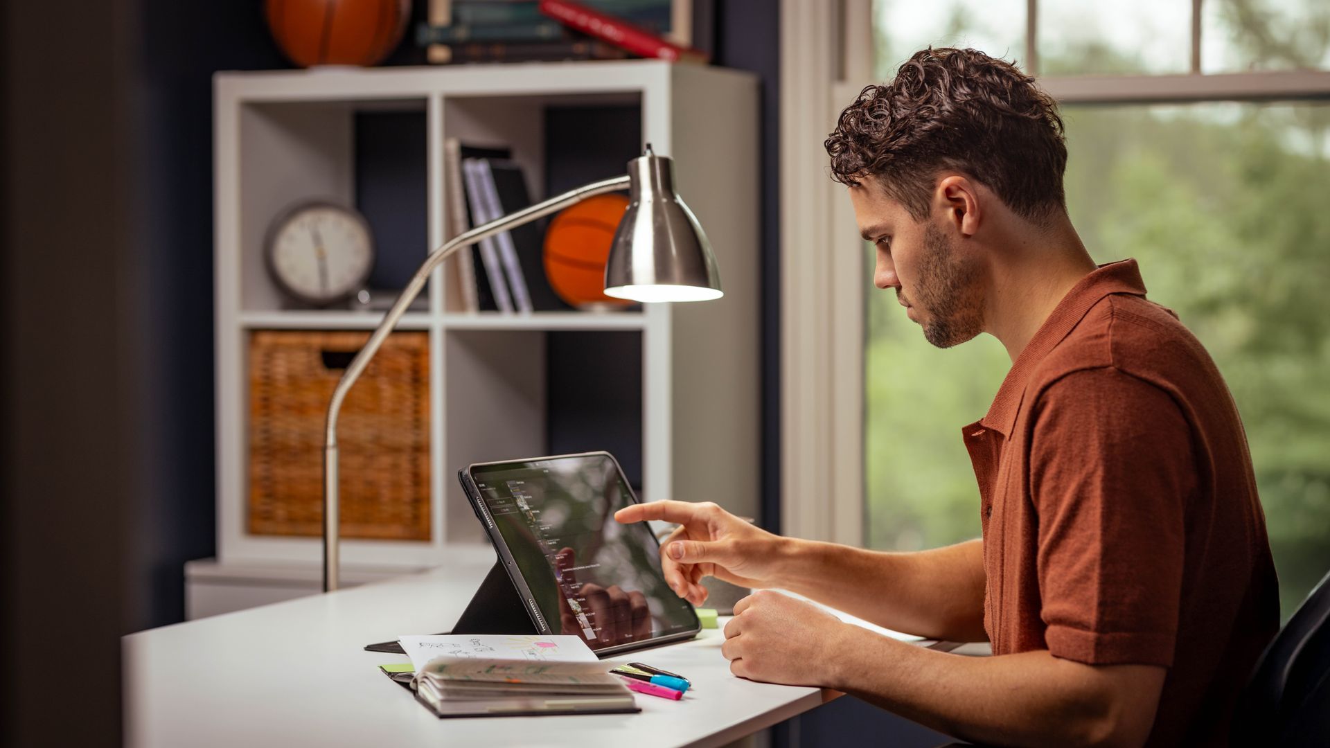 Seorang saudara muda melakukan pelajaran pribadi dengan menggunakan Alkitab, tablet, dan buku catatan. Dia membuat catatan di Alkitabnya.