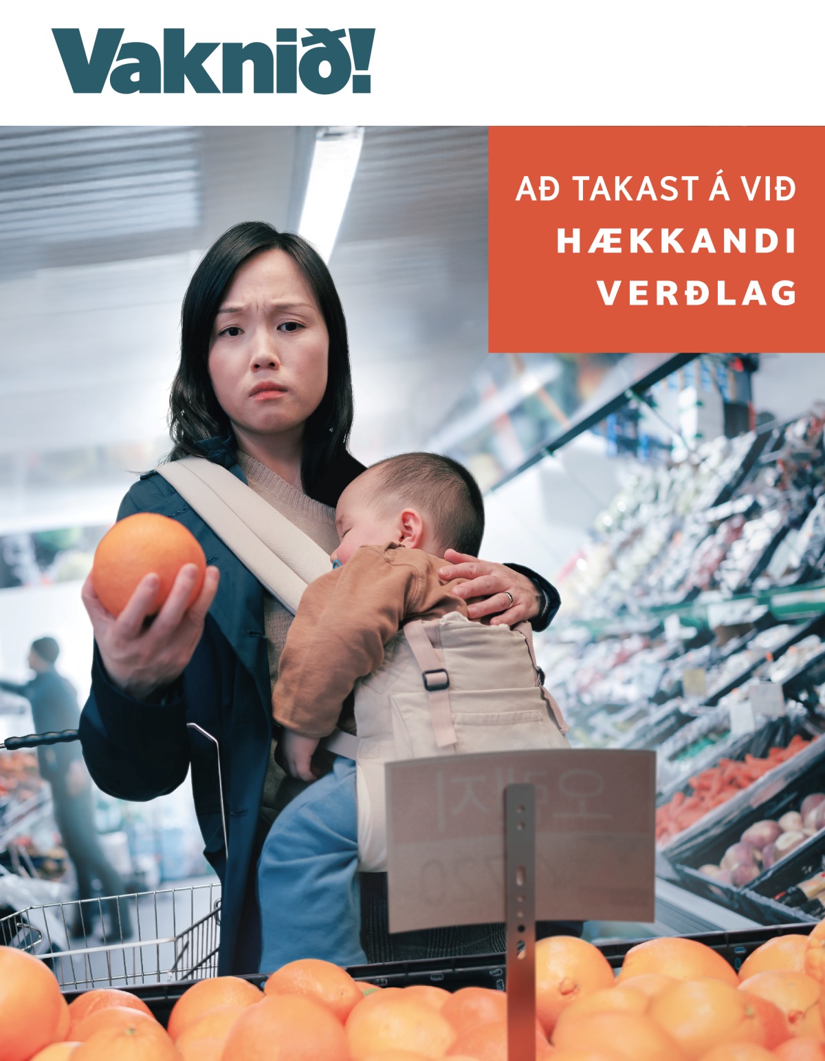 Móðir horfir áhyggjufull á verð á ávöxtum í matvörubúð. Hún er með sofandi barn í burðarpoka framan á sér.
