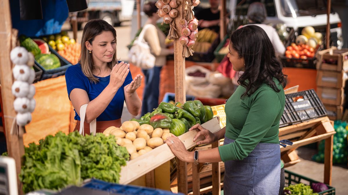 Al mercato, la sorella dà un biglietto da visita del sito jw.org a una commerciante.