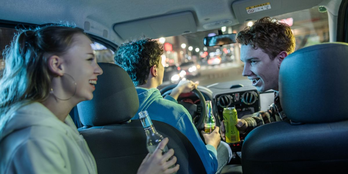 Dei ragazzi in auto, compreso quello che sta guidando, bevono alcolici.