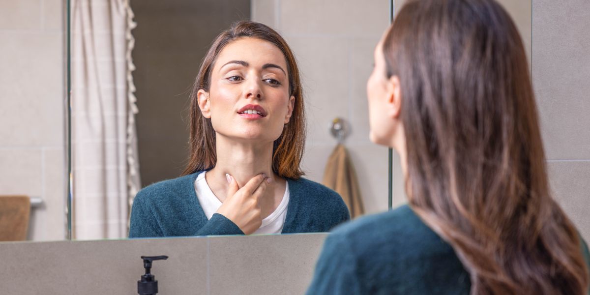 Una donna davanti allo specchio si tocca il collo per controllare la tiroide.