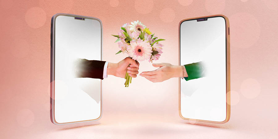Gli schermi di due smartphone uno di fronte all’altro. Da uno fuoriesce la mano di un uomo con un mazzo di fiori, e dall’altro fuoriesce la mano di una donna che lo accetta.
