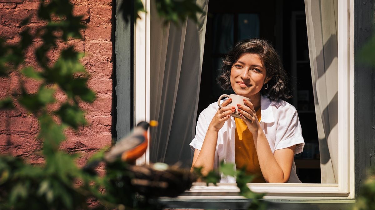 Una sorella, sorridente, osserva un uccellino dalla sua finestra.