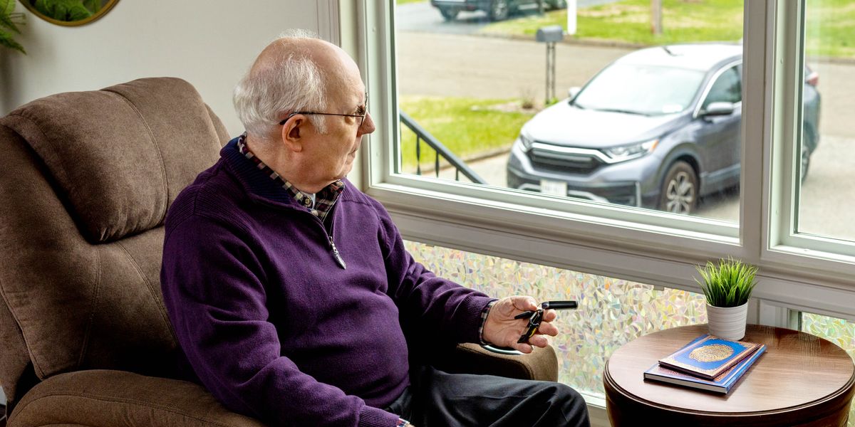 Un fratello avanti negli anni è seduto vicino alla finestra e guarda la sua auto parcheggiata fuori. Ha in mano le chiavi dell’auto e riflette.