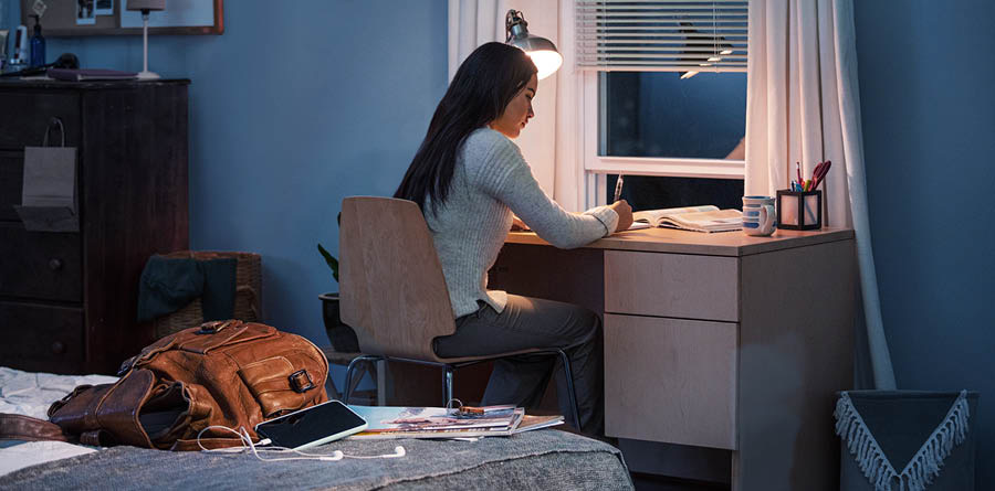 女の子が自分の部屋の机で勉強している。リュックとスマホと雑誌は後ろの視界に入らない所に置いている。